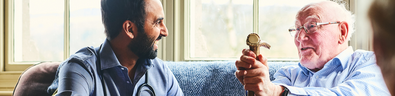 Caregiver with stethoscope engaging with a senior holding a cane