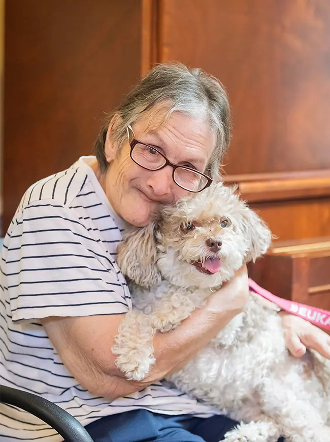A happy resident of ActivCare cuddles a dog.